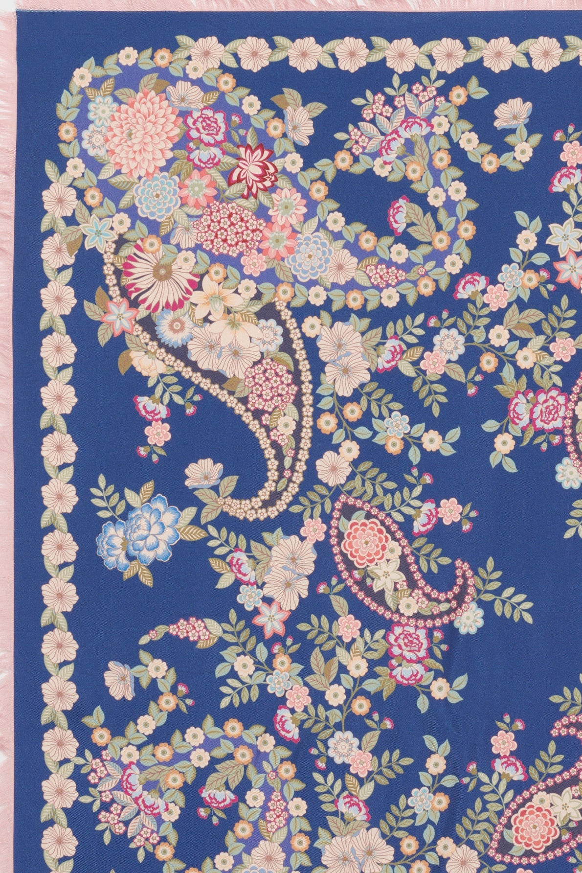 A blue fabric with intricate paisley and motif floral patterns in cream, pink, red, and light blue, bordered with a fringe on the left edge—a perfect choice for a carré en soie.