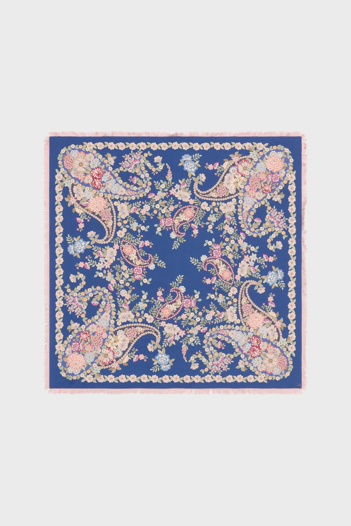 A square blue carré en soie scarf featuring an ornate floral and paisley pattern in pink, yellow, and green, bordered by a pink fringe and an intricate motif floral design.