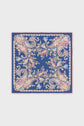 A square blue carré en soie scarf featuring an ornate floral and paisley pattern in pink, yellow, and green, bordered by a pink fringe and an intricate motif floral design.