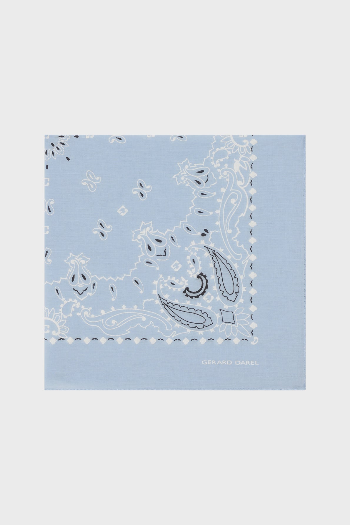 Light blue square bandana with a white and black paisley pattern and scalloped edges. Crafted in soft foulard coton, this carré Dayana features the name GERARD DAREL in white text near the lower right corner.