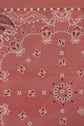 Red bandana fabric with a paisley pattern and white, black, and pink ornamental shapes arranged symmetrically across the surface. This foulard coton features floral, geometric, and abstract elements in an élégant imprimé bandana style for a vibrant, eye-catching look.
