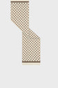 A patterned beige and brown carré soie scarf is folded diagonally, forming a zigzag shape. This édition limitée accessory features a repeating hexagonal motif reminiscent of a subtle monogramme GD and two thin brown borders at the bottom edges.