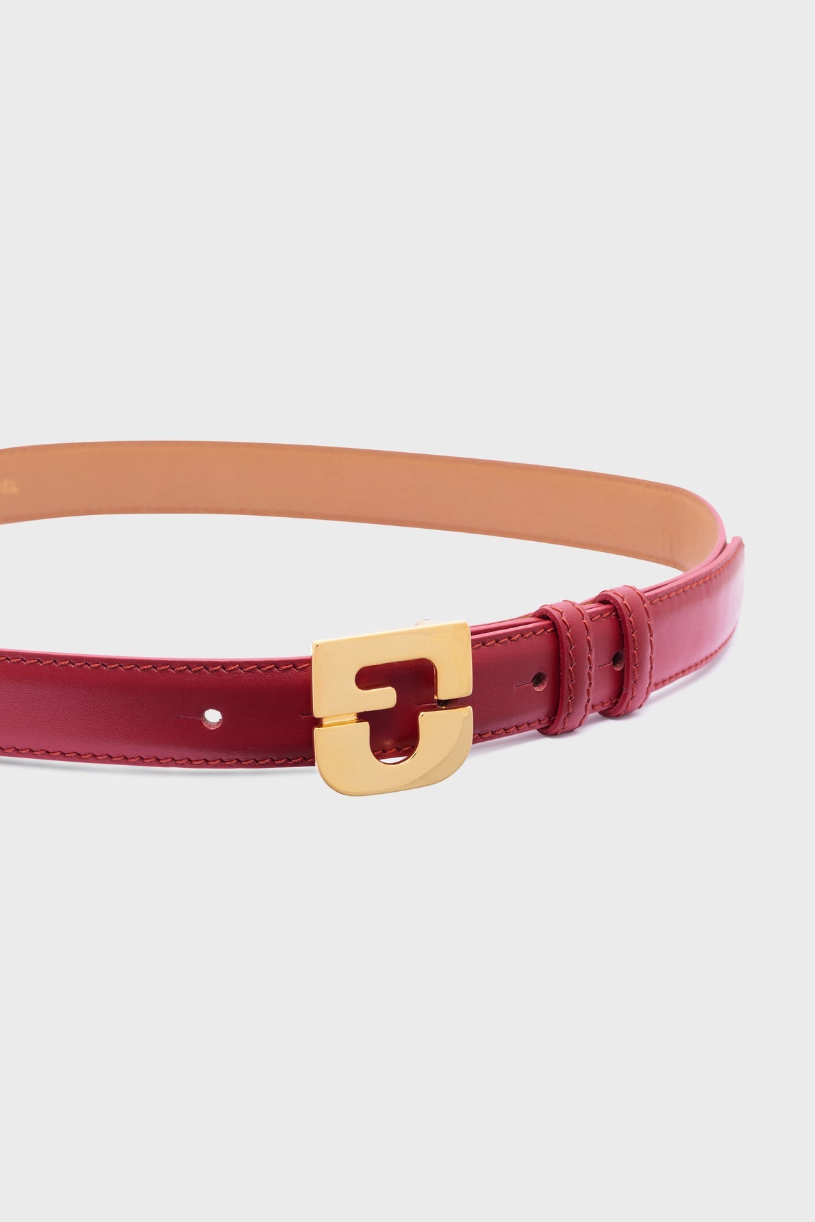 A red leather belt (ceinture en cuir) with a gold rectangular buckle, shown against a plain white background, exemplifies Gerard Darel’s signature style in ceinture femme accessories.