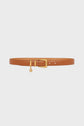 A tan leather belt with a gold rectangular buckle and a small gold charm hanging from the buckle, this ceinture élégante by Gerard Darel is displayed on a plain white background.