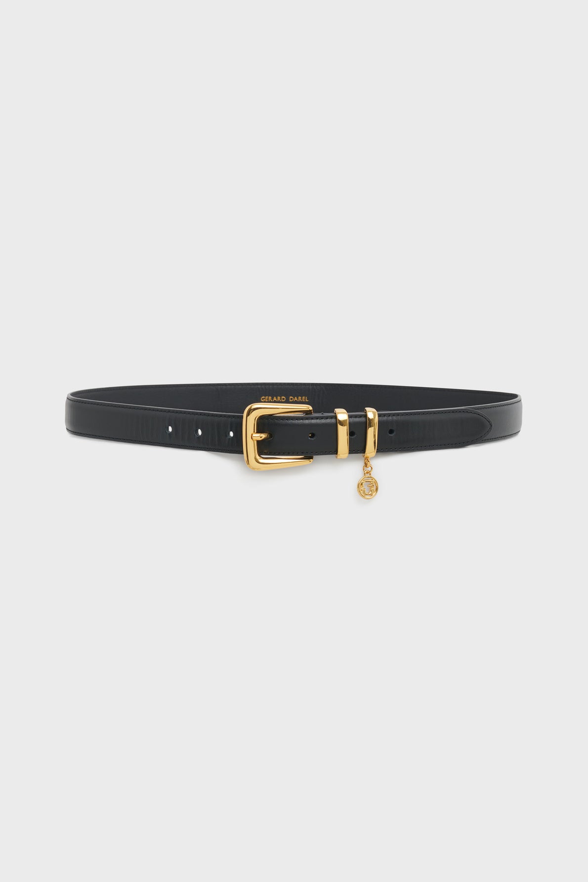A black leather ceinture Gérard Darel with a gold buckle and a small round gold charm hanging from the buckle, displayed on a plain white background—an undeniably élégante ceinture femme for any sophisticated wardrobe.