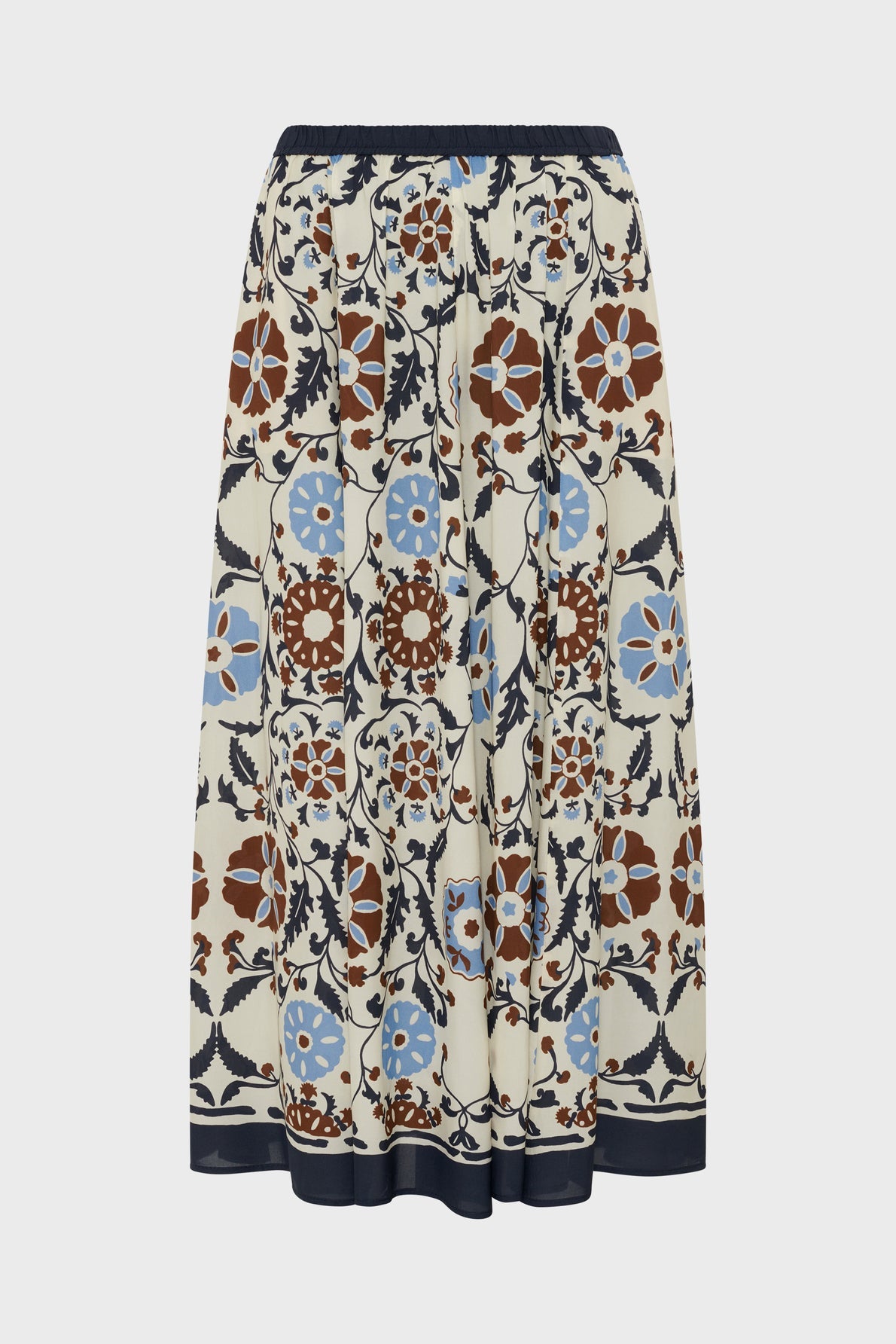 A jupe longue with an elastic waistband, featuring a geometric floral motif végétal in brown, blue, and navy on a cream background. The forme évasée adds effortless movement to the skirt’s design.