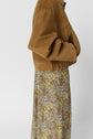 A person wearing a tan suede jacket with gathered cuffs and hem, paired with a jupe longue à motif floral. The image is cropped, showing only the side of the torso and lower body against a plain background, evoking un esprit bohème.