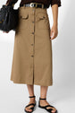 A person wearing a tan, button-front midi skirt with flap pockets, a black belt, and black strappy sandals, holding a textured black handbag.