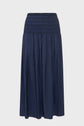 A navy blue, ankle-length skirt with a wide, smocked elastic waistband and a slightly crinkled, flowy fabric. Reminiscent of a classic jupe bleu marine, the skirt hangs straight and has a simple, elegant design against a plain background.