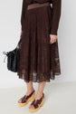 Person wearing a brown lace midi skirt, dark brown blouse, wooden platform sandals, and holding a black handbag. The outfit is stylish and the background is plain white.