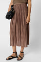 A person wearing a brown sleeveless top, a pleated brown midi skirt, black flat sandals, and holding a small black handbag. The outfit is casual and neutral-toned.