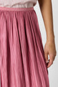 A person wearing a pink pleated skirt and a white shirt with thin red stripes. Only the lower torso and right arm are visible.