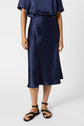 Person wearing a dark blue satin midi skirt, navy top, and black sandals, standing against a plain white background. Upper body is partially out of frame.