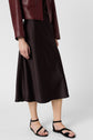 A person wears a burgundy leather jacket, a dark brown midi skirt, and black strappy sandals against a plain light background.
