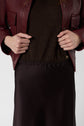 A person wearing a burgundy leather jacket over a dark brown top and skirt, holding the jacket open with both hands. The image is cropped to show only the torso and hands.