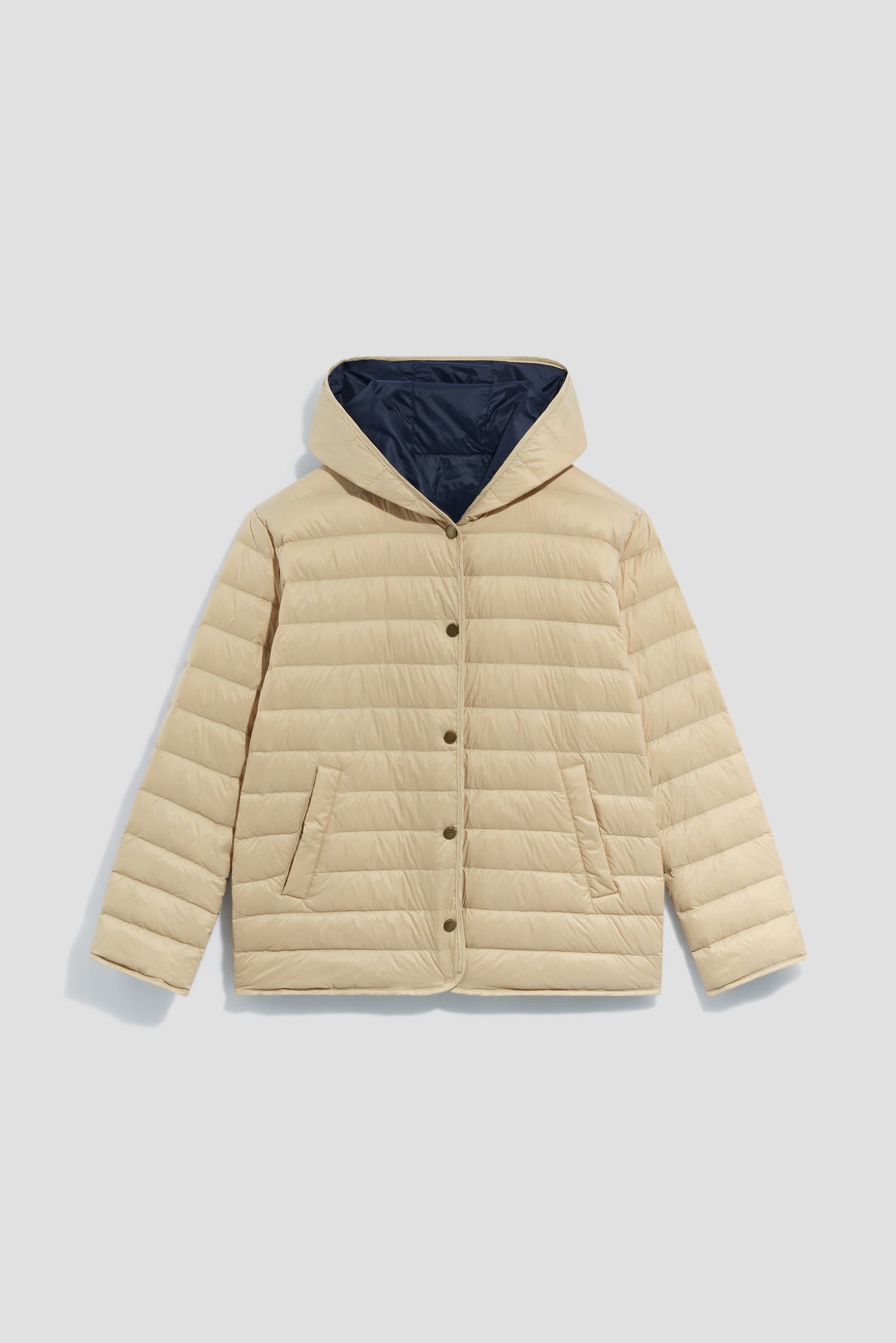 Beige puffer jacket with a hood (capuche), front snap buttons, and two front pockets. This parka courte features horizontal quilting and a contrasting dark blue lining inside the hood.