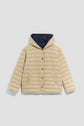 Beige puffer jacket with a hood (capuche), front snap buttons, and two front pockets. This parka courte features horizontal quilting and a contrasting dark blue lining inside the hood.