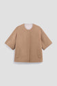Camel-colored, short-sleeve, collarless manteau court crafted from luxurious laine double face, featuring front patch pockets, a straight hem, and a minimalist open-front design, displayed on a plain light background.