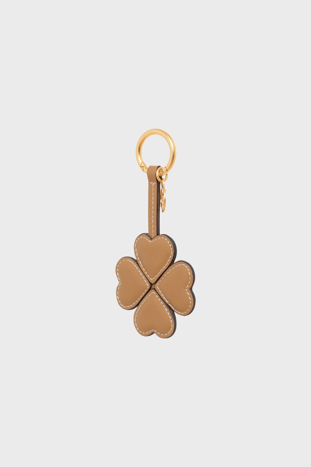 Tan leather porte-clé trèfle shaped like a four-leaf clover, with each leaf formed by a heart. This elegant porte-clé cuir is attached to a gold keyring and clasp, set against a plain light background.