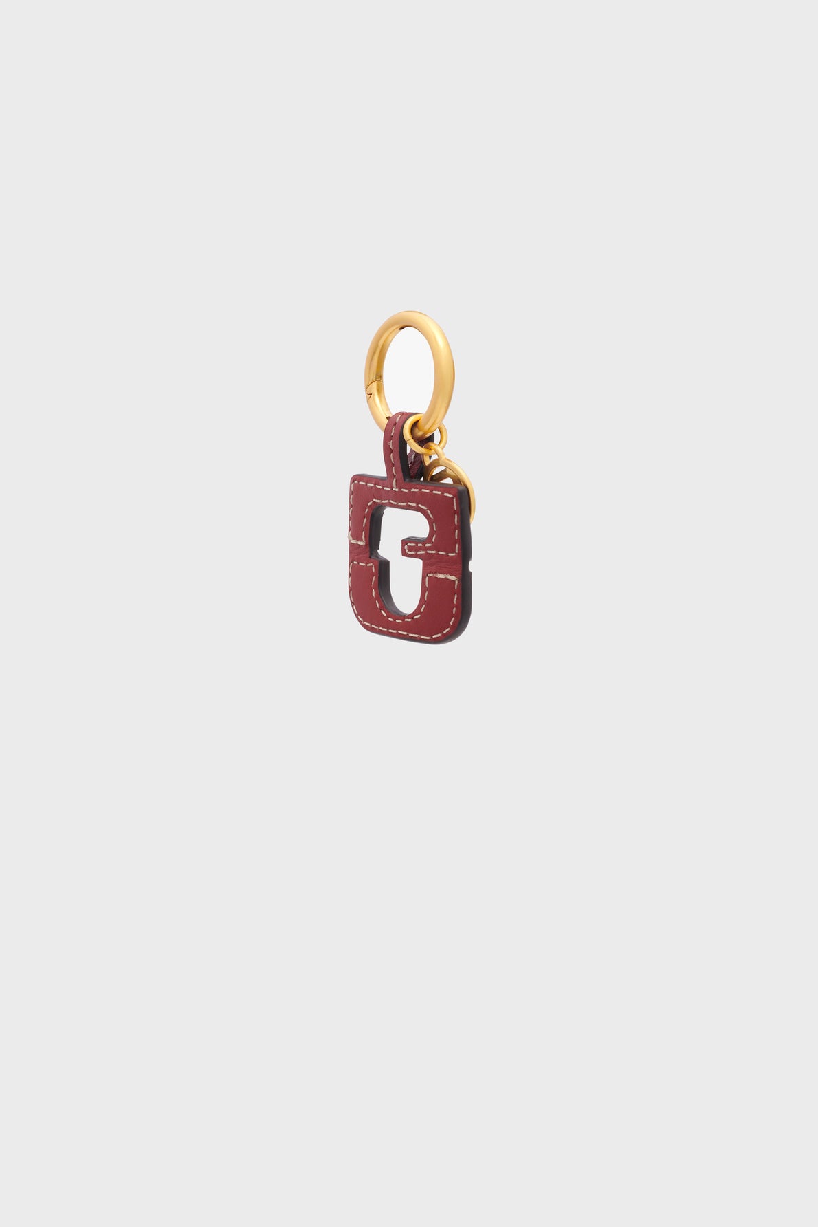 A small, gold keyring with a burgundy Gerard Darel porte-clé en cuir charm featuring a cut-out square design and white stitching, set against a plain light gray background.