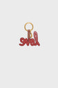 A red leather porte-clé LOVE, shaped in elegant cursive and crafted from cuir de vachette, is attached to a gold keyring with a brown leather loop, set against a plain white background.