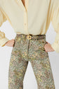 Person wearing a pale yellow blouse tucked into high-waisted, motif floral pantalon flare with a gold-buckled belt, hands on hips, shown from shoulders to knees against a white background.