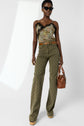 Woman wearing sunglasses, a floral and lace camisole, olive green patterned pantalon monogramme high-waisted pants, a brown belt, holding a brown handbag, and platform shoes, poses confidently against a plain light background.