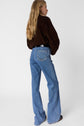 A person with long blonde hair wears a dark brown jacket and light blue jean ANNA coupe flare taille haute, standing with their back turned against a plain white background.