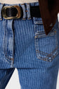 Close-up of a person wearing blue pinstriped jeans with orange stitching, featuring a taille haute fit and a coupe flare silhouette from the jean ANNA collection, paired with a black belt with a gold buckle and part of a brown jacket visible at the top right.