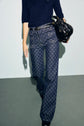 A person wearing high-waisted, wide-leg jeans with a motif monogramme, a navy textured top, and carrying a black handbag. The image does not show the person’s face.
