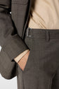 Person wearing a beige shirt and gray suit with one hand in their pocket. The suit features a metal side adjuster on the waistband, and the pantalon droit is tailored in a taille haute style. Only the torso and upper legs are visible.