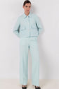 A person stands against a white wall, wearing a light blue pantalon de tailleur in lin mélangé with a cropped jacket, wide-leg trousers, and black heels—a sophisticated tenue de bureau perfect for modern professionals.
