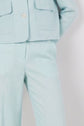 Person wearing a light blue lin mélangé suit with large front pockets and button detail on the jacket, standing with arms behind their back. Only the torso and legs are visible; the head and feet are not shown, highlighting the élégant pantalon de tailleur—perfect for une tenue de bureau raffinée.