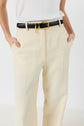 Person wearing cream-colored pantalon tailleur femme, a white shirt, and a black belt with a large gold buckle, with hands in pockets—perfect for a tenue bureau chic.