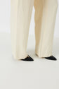 A person wearing wide-leg cream pants reminiscent of a pantalon tailleur femme and black pointed-toe flats with a gold detail, standing on a white surface—an effortlessly tenue bureau chic look.