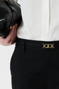 A person wearing a white shirt and a pantalon noir coupe droite longueur 7/8 with a gold belt buckle, holding a black leather handbag.