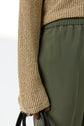 A person wearing an olive green pantalon fluide à taille élastiquée or a skirt and a beige knit sweater holds a black handbag, visible from the waist to mid-thigh.