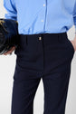 Person wearing a light blue button-up shirt and dark navy trousers with one hand in a pocket, holding a black handbag in the other hand. The image is cropped to show from mid-torso to mid-thigh.