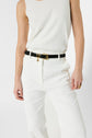 A person wearing a sleeveless white top, white pants, and a black belt with a gold buckle stands against a plain background. Their right hand rests by their side, and their left hand is slightly bent.