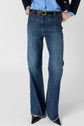 Person wearing blue flared jeans with frayed hems, a black belt, a light blue shirt, and a dark blazer. Black pointed-toe shoes are visible. The image is cropped at the waist and ankles.