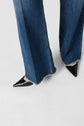 A close-up of a person wearing wide-leg blue jeans with frayed hems and black pointed-toe shoes on a light gray floor.