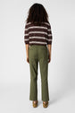 Person standing facing away, wearing a brown and white striped shirt, olive green pants, and brown shoes, against a plain white background.