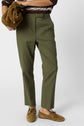 Person wearing olive green trousers, brown suede loafers, and a brown sweater with white stripes, holding a brown textured bag against a plain background.
