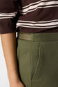 A person wearing a brown and white striped top and olive green pants with an elastic waistband and side pocket, shown from the waist to mid-arm.