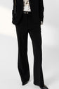 Person wearing a black blazer and pants, white shirt with black graphic, black belt, and pointed black shoes. The look is elevated with a pantalon noir femme that offers both sophistication and modern style. Their hands are in their pockets, and their head is not visible in the image.