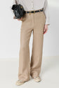 Person wearing beige wide-leg trousers, a striped button-up shirt, and white sneakers, holding a black handbag. The outfit has a casual and stylish look. Only the body from shoulders down is visible.