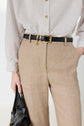 Person wearing a white pinstriped shirt tucked into beige pants with a black belt, holding a black handbag, and one hand in their pocket.