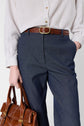 A person wearing a striped button-up shirt tucked into a pantalon denim bleu foncé taille haute with a brown leather belt, holding a matching brown leather handbag.