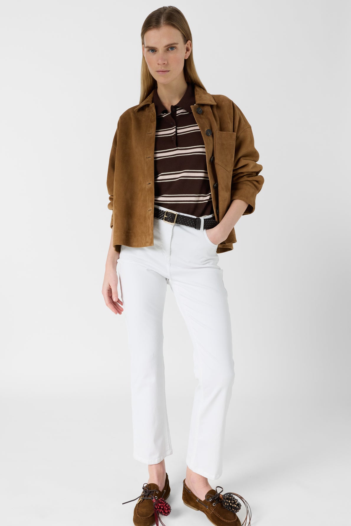 A woman stands against a white background wearing a brown suede jacket, a dark brown and white striped top, and coupe slim jean blanc in coton stretch, paired with brown loafers with decorative bows. She has straight blonde hair and a neutral expression.