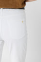 A person wearing a brown top and a jean blanc in a coupe slim fit. The image focuses on the back pocket of the jeans, crafted from coton stretch and adorned with a small gold emblem.